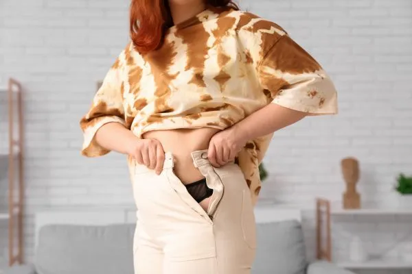 Image of woman trying to do her trousers up after pregnancy weight gain Streatley