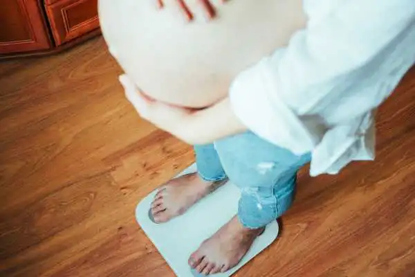 Image of woman weighing herself and experiencing weight gain through pregnancy Streatley