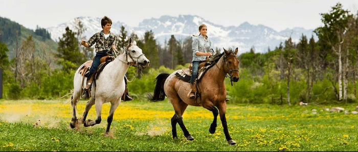 Confident plus-size woman riding Streatley a horse through a field with a smile on her face.